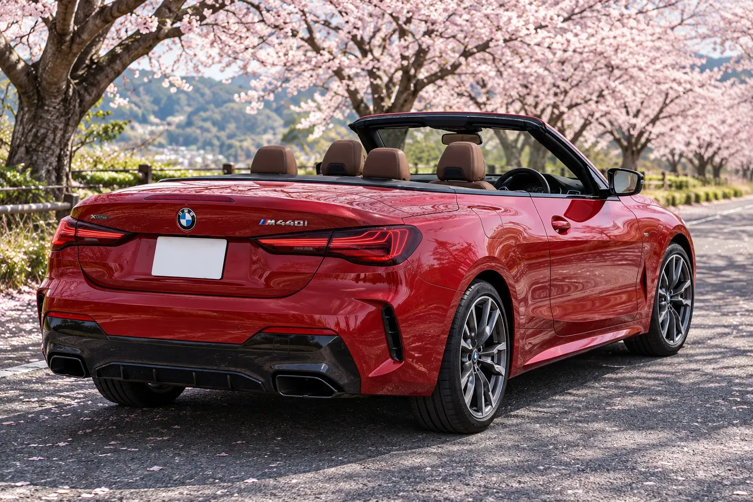 BMW 4シリーズ カブリオレ（G23型・改良後）M440i xDriveの屋根を開けた状態を斜め後ろから見た実車イラスト。ファイヤー・レッドのボディ、黒い電動ソフトトップを収めた後部、横長のLEDテールランプ。春の桜並木の道