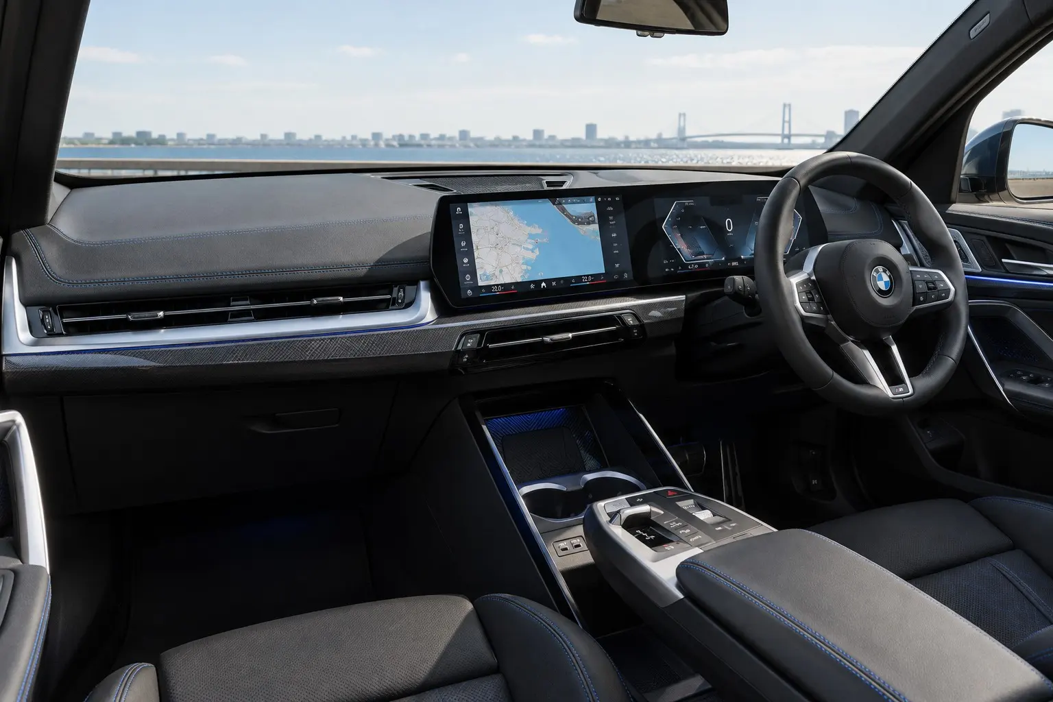 BMW iX1(U11型)の運転席まわりの実車イラスト。日本仕様の右ハンドル。横に長い曲面ディスプレイ、浮いたようなセンター・アームレスト、M Sportのステアリング、青いアクセントの内装