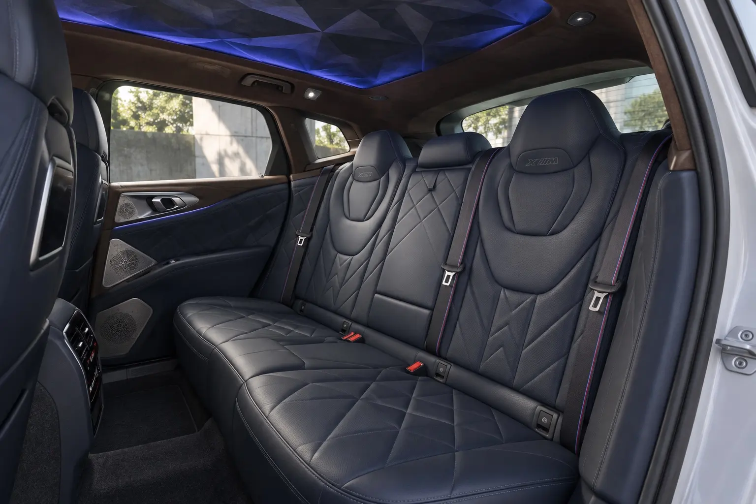 BMW XM（G09型）の後席の実車イラスト。ひと続きになった濃い色の革のシート、ダイヤモンド形のヘッドレスト、立体的なプリズム模様の天井、柔らかな間接照明。シートの上にクッションや枕は置かない