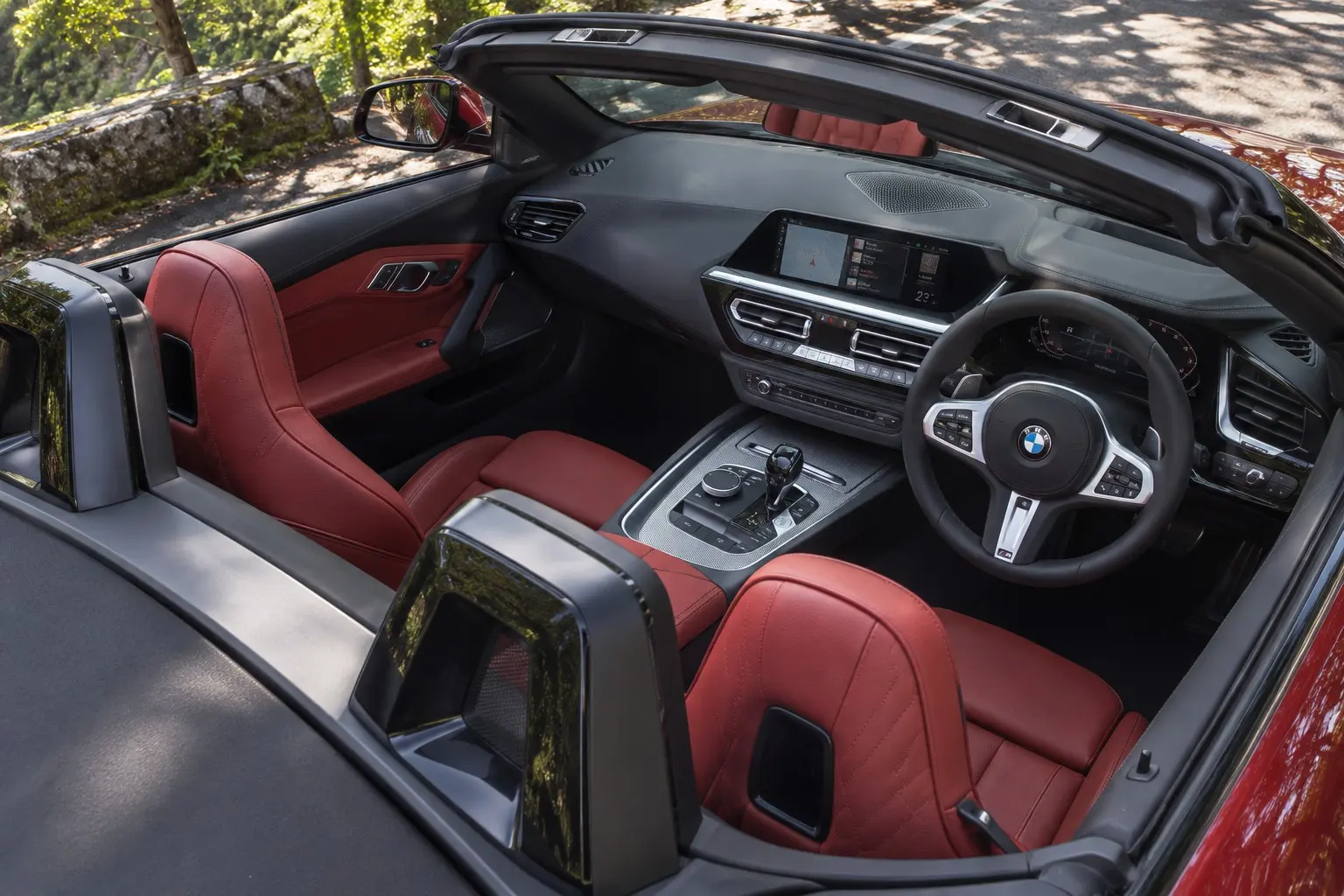 BMW Z4(G29型)の運転席まわりを、屋根を開けた状態で上から見た実車イラスト。日本仕様の右ハンドル。マグマ・レッドのヴァーネスカ・レザーのシート、Mスポーツ・ステアリング、10.25インチの2つの画面、ロール・バー。木漏れ日の差す山道