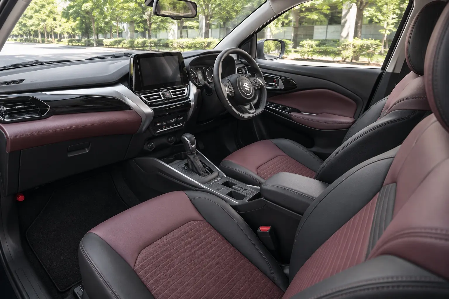 運転席側から見たスズキ フロンクスの前席。ボルドーとブラックのシート、センターコンソール。窓の外は街路樹、昼の自然光