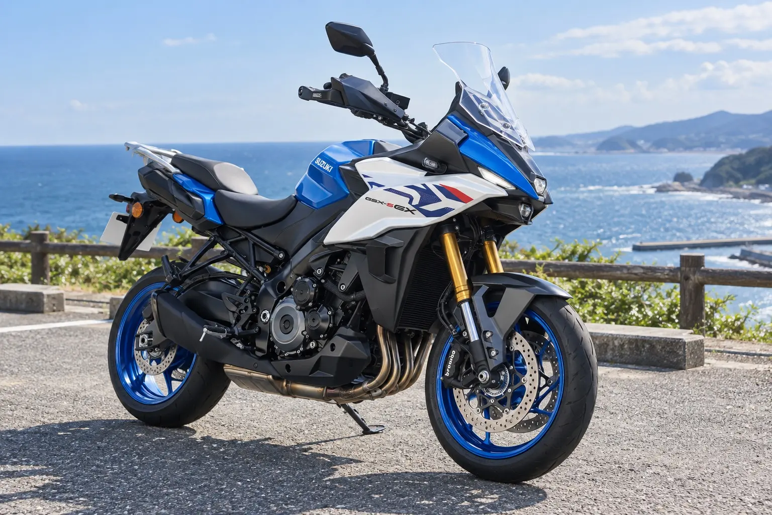 スズキ GSX-S1000GXを斜め前から見たカット。白と青の車体、高めのスクリーン、ナックルガード、リヤキャリア、直列4気筒エンジン