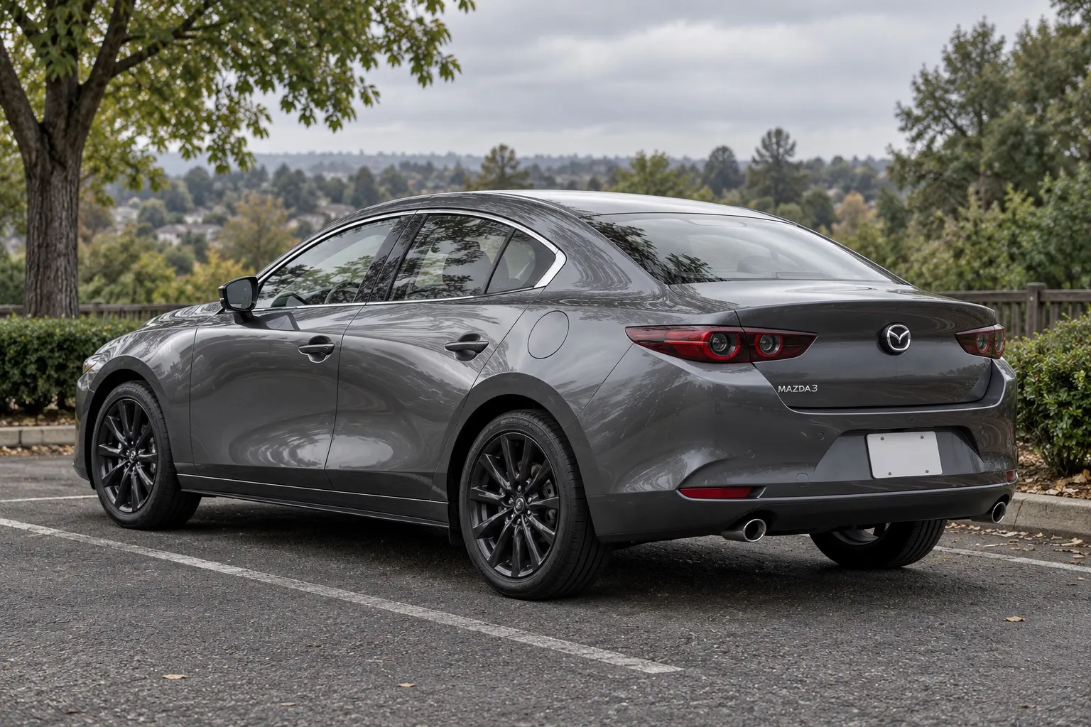 マツダ MAZDA3 セダン 25L(2026年改良後)の斜め後ろからの外観。ボディカラーはマシーングレープレミアムメタリック。郊外の並木道の駐車スペース